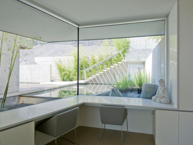 Corner desk space has been built-in below the large wrap around windows of this minimalist home office for two. The white and grey used in this room match the home decor throughout the house.