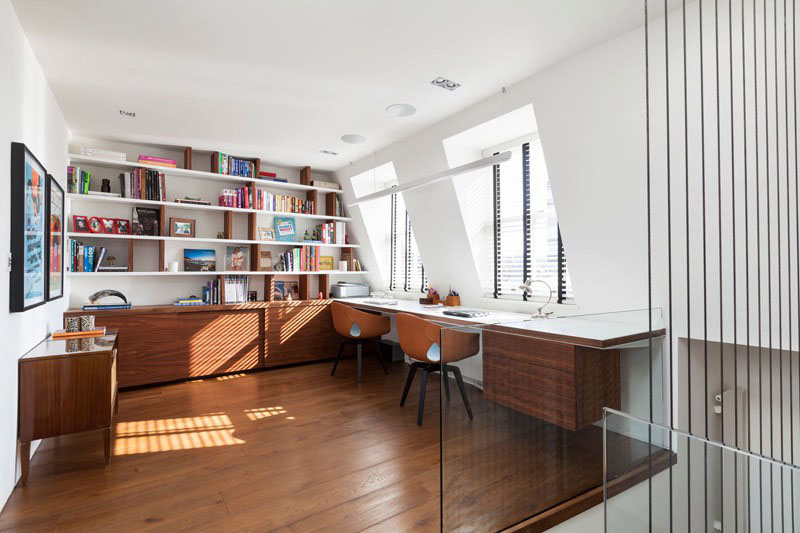 At the top of a flight of stairs, this home office has built-in shelves and cabinets providing excellent storage. The floating desk provides a shared work area and faces two individual windows that look outside.