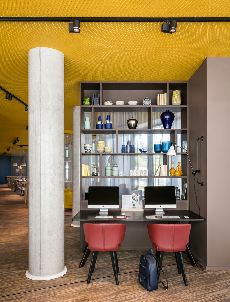 In this modern hotel, a small work area has been set up with two computers, while a bookshelf provides a backdrop and separates the work area from another sitting areas.