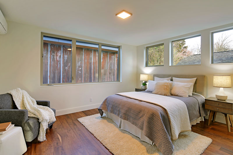 The bed in this modern bedroom sits underneath and beside windows, providing lots of light. Two wood nightstands with lamps compliment the walnut floor and colors used in the room. 