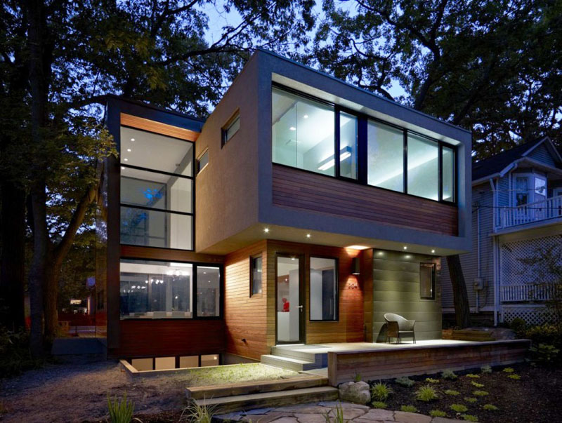 A stone pathway through the garden leads to the entrance of this modern house, which cantilevers out providing coverage for a small patio area.