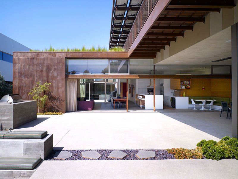 At the rear of this modern house, a large concrete patio is revealed with a 40 foot long glass sliding door that leads to the inside of the house.