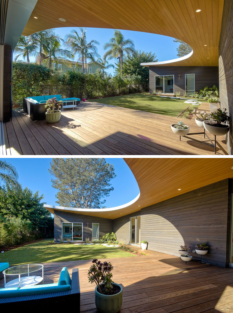 Looking out on this modern wood patio, a curved roof with hidden lighting is revealed. Bright blue patio furniture provides a nice place to lounge outside.