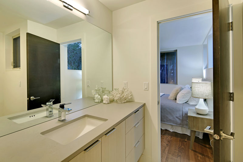 This modern ensuite bathroom is minimally decorated with a light colored counter and cabinet with simple drawer pulls. A large rectangular mirror helps to make the bathroom feel larger and brighter.