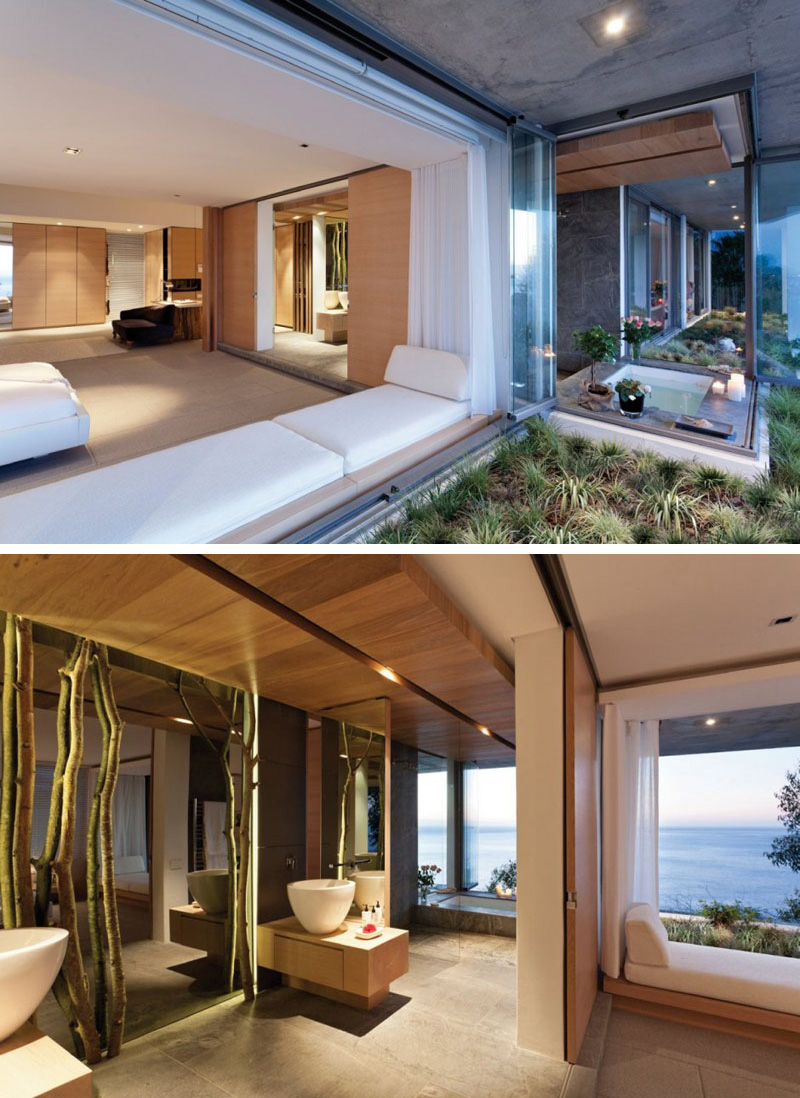 The bathtub in this modern master bathroom is surrounded by windows, providing an uninterrupted water view. Two large, white counter top sinks are situated beside a floor-to-ceiling mirror that is framed by portions of trees.