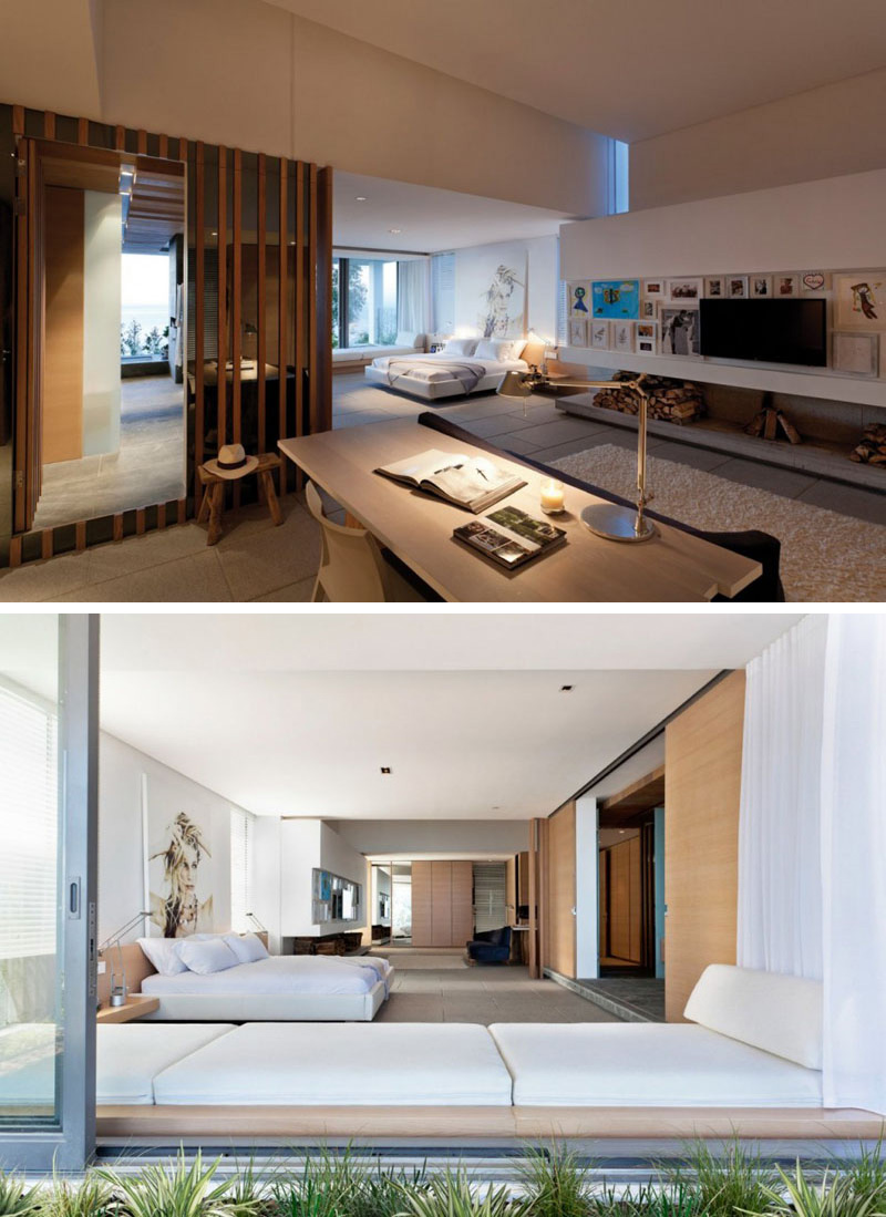 This modern master bedroom shares space with a small home office. The interiors have been kept mostly white, with light wood accents used throughout. A white upholstered window seat is perfect for reading and daydreaming.