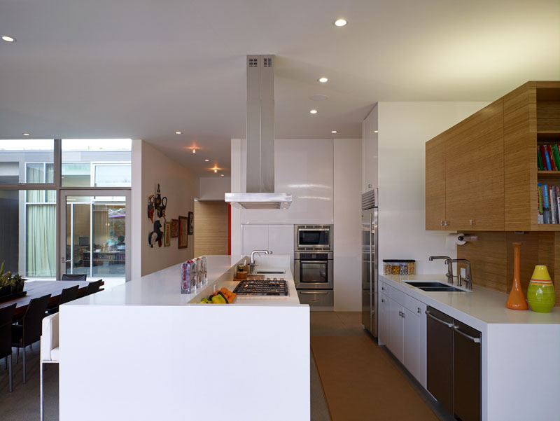 A large wood dining table separates the living room from this modern kitchen. In this kitchen, a long white island is combined with wood cabinetry to provide a contemporary look.