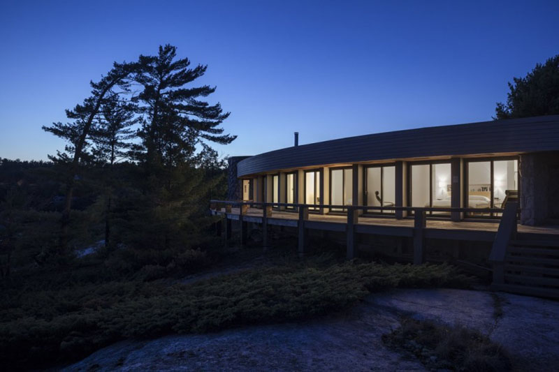 Altius Architecture have given this 1970's lakeside home, a modern house renovation in Parry Sound, Canada. A semi-circle floor plan with an open layout are used along with, clean white interiors and various lighting to keep the house light and airy.