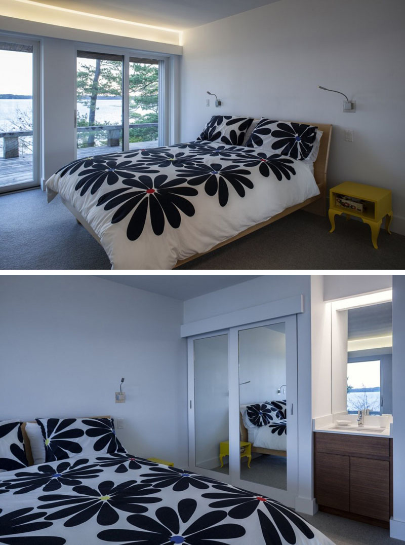 The large floral print blanket and yellow nightstand add a pop of color in this modern bedroom. A mirrored closet with sliding doors is placed beside a small sink with wood cabinets. Glass sliding doors with hidden lighting above lead to the wood balcony of the house.