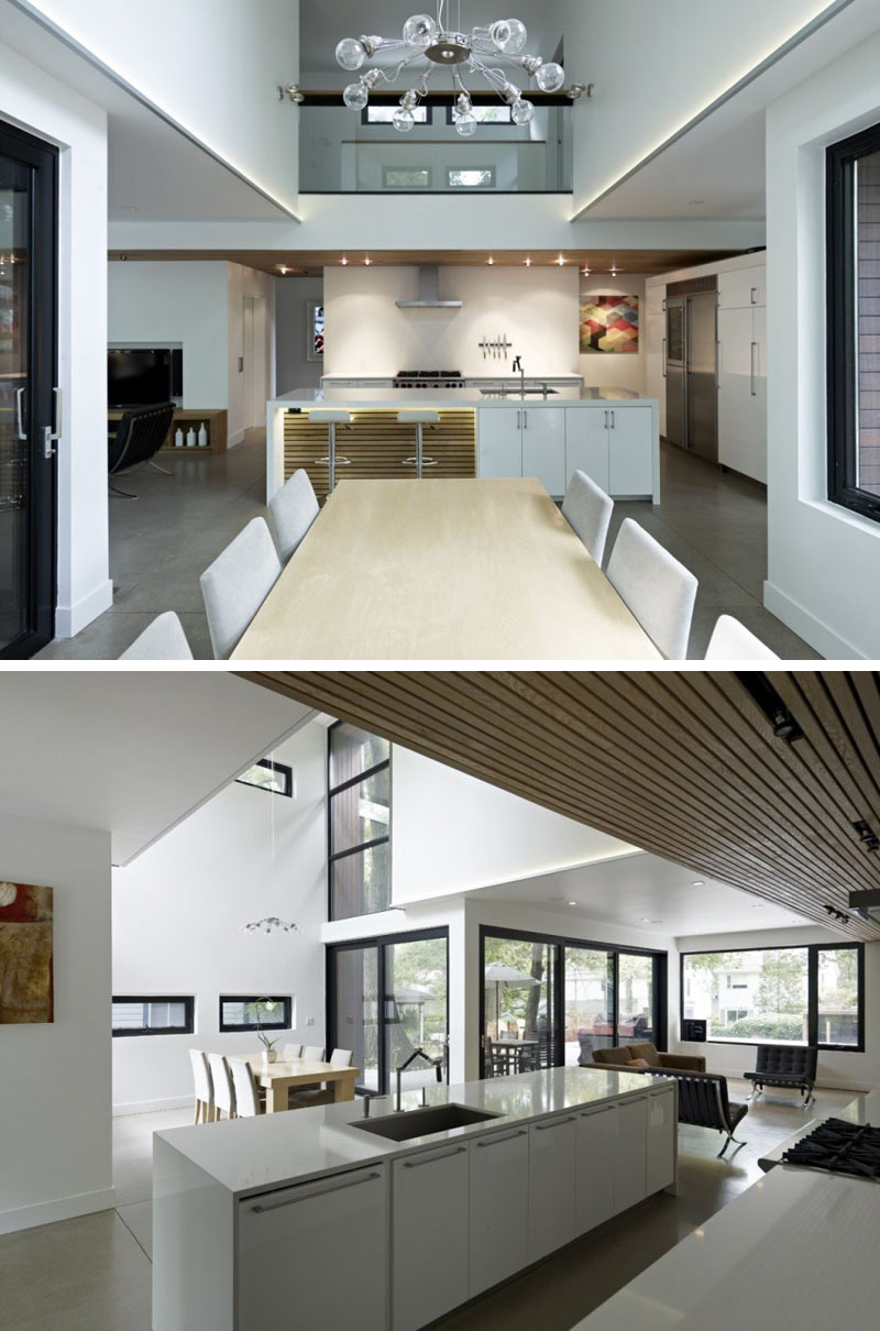 In this modern dining room, a unique chandelier with exposed bulbs hangs above the long wood dining table. The surrounding windows in this double height room make the space light and airy.