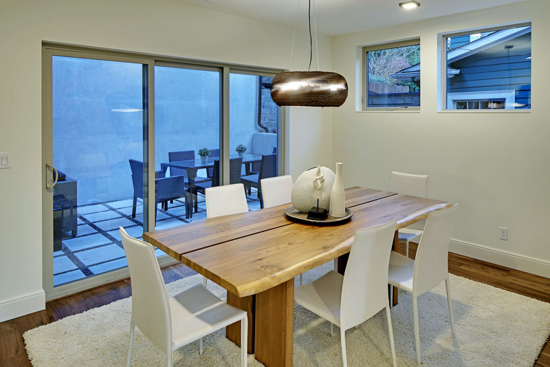 In this modern dining room, a wood table sits on a white area rug and is surrounded by white chairs. A handmade pendant light hangs above the table that compliments others through the home. 