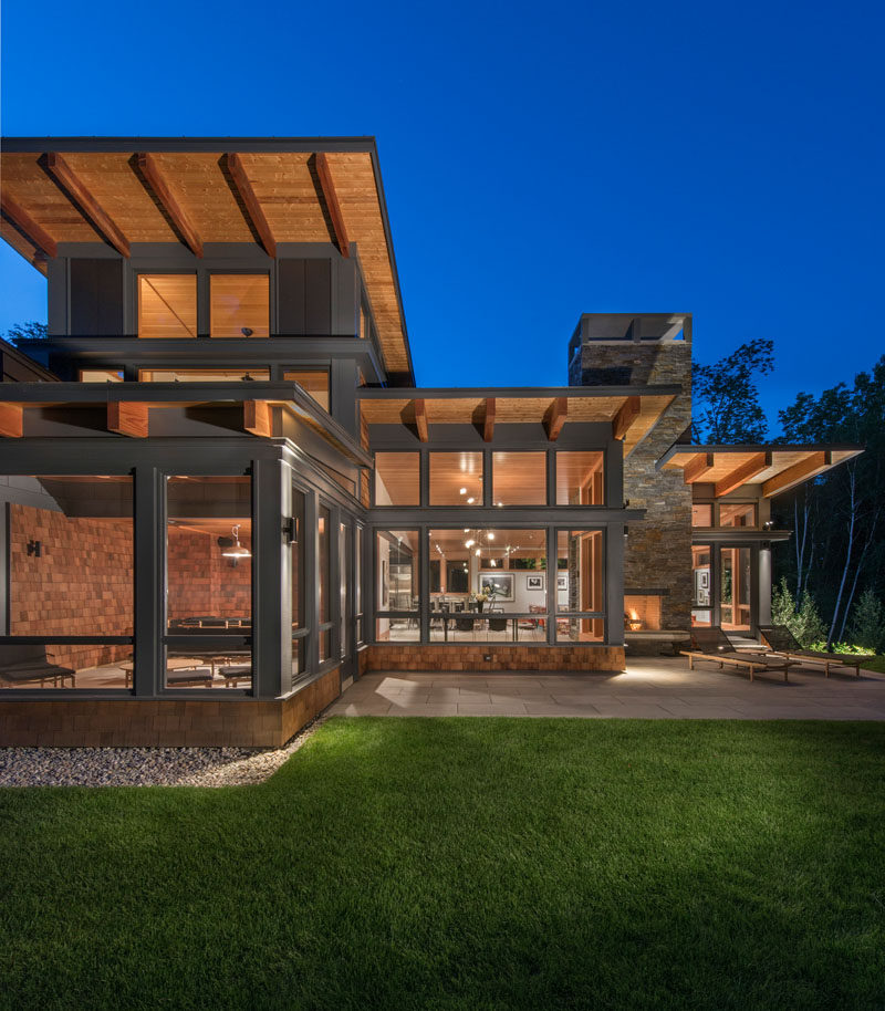 This modern house has a backyard patio with sun loungers and an outdoor fireplace. From this angle, you can see that the roof is sloped, this was a request of the home owner to make sure that the snow / ice doesn't build up in the winter. The sloped roof also maximizes passive solar heating in the winter, and the generous overhangs protect from summer sun.