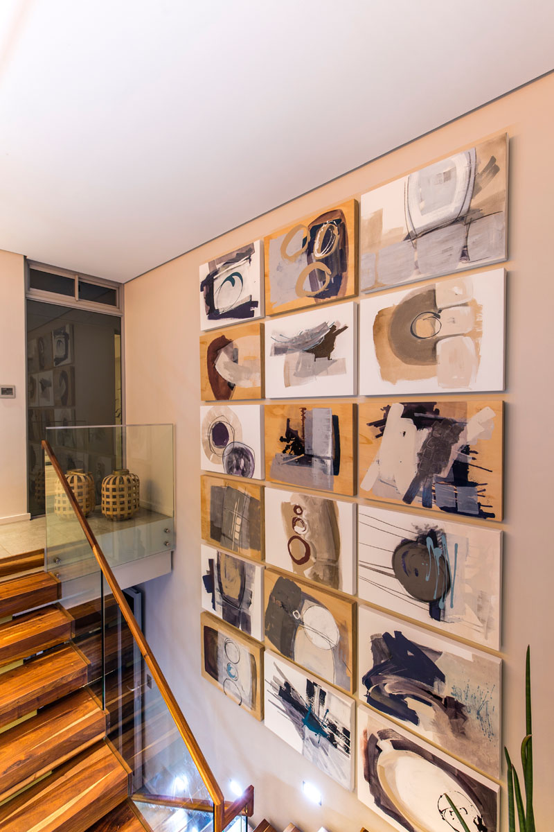 This set of modern wood stairs leads down from the dining room into the entertainment areas of the house. Decorative art pieces fill the wall that leads downstairs.