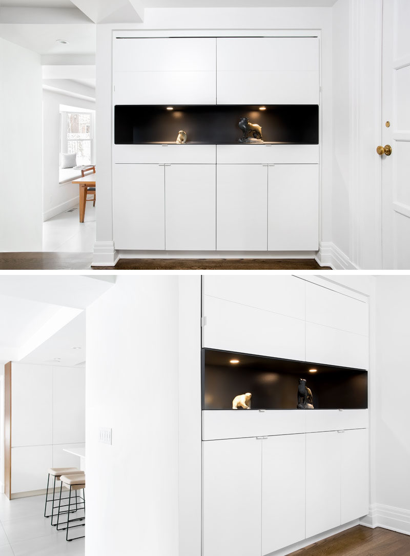 This entryway has been updated with a wall of white cabinets, with the middle section painted black to create a dramatic backdrop for highlighted artworks.