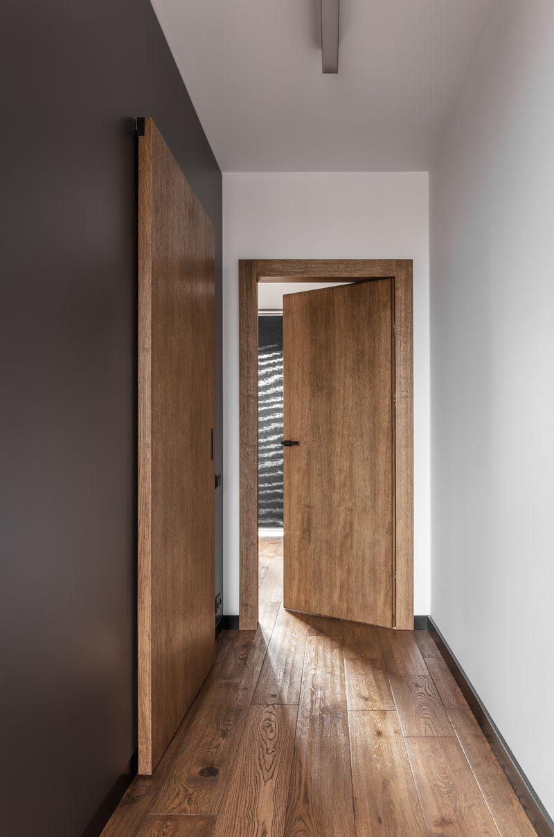 This contemporary apartment features wood doors, dark grey accent walls and wood flooring.