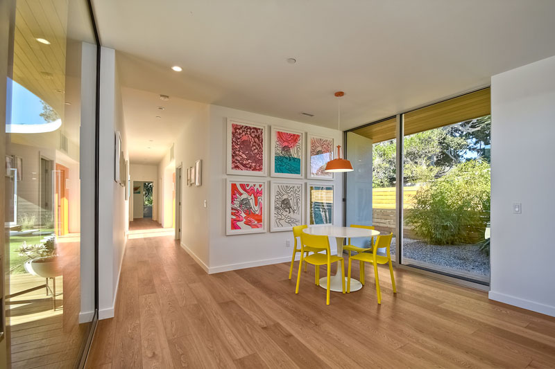 In this modern breakfast nook, a white table with yellow chairs, sits below a bright orange pendant lamp. A sliding glass door provides easy access to outside.