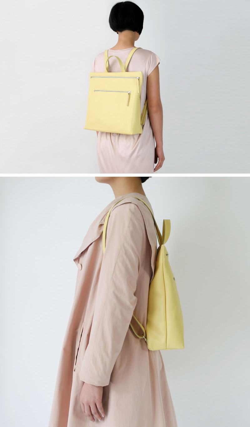 This modern yellow leather backpack has two large silver zippers, and a handle at the top. 