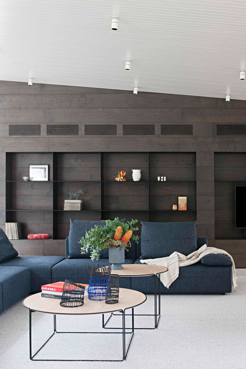 This modern living room has a light colored concrete floor, a dark blue couch and a large black bookshelf with dark wood.