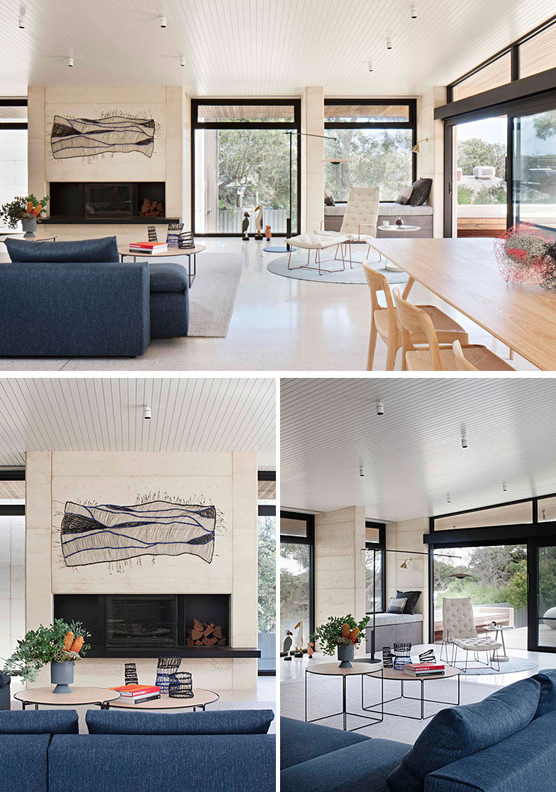 This modern living room is focused on a fireplace, while the dark blue couch is adds a touch of color to the interior. Black framed aluminium doors and windows fill the open room with plenty of natural light.