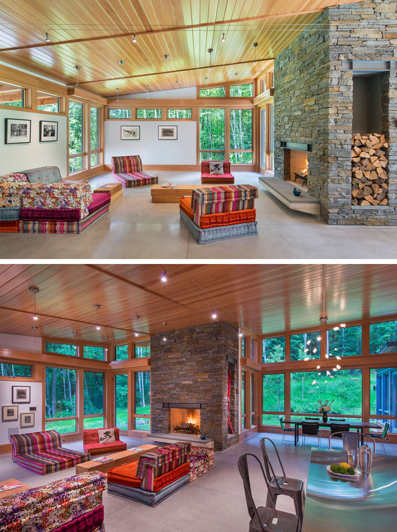 In this modern living room, bright colored seating and a fireplace with a stone surround creates a relaxing environment. Natural light floods the interior through the numerous windows, some of which have been designed to follow the roof line.