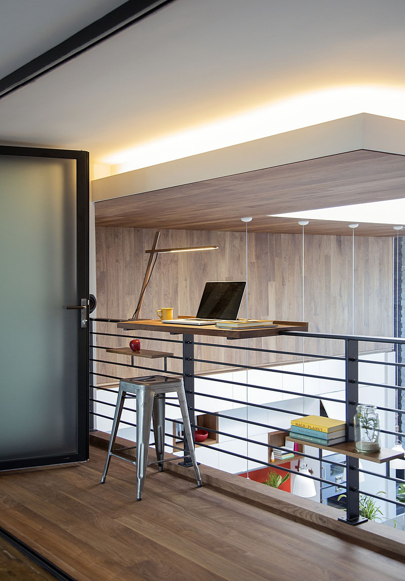 A wood desk has been attached to a black railing to create a work space that can easily view the lower level of this modern loft. Hidden lighting in the ceiling provides an extra glow to this modern lofted level.