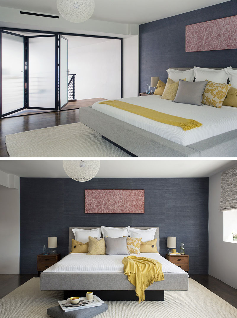 In this modern master bedroom, opaque folding glass doors provide privacy separating it from the rest of loft. The light grey, soft framed bed sits in front of a dark colored accent wall. 