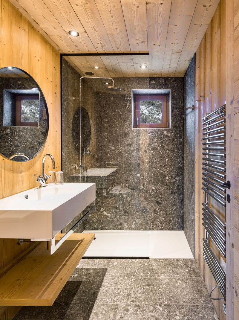 In this rustic modern bathroom, wood walls and ceiling have been paired with stone tiles and a glass shower partition.