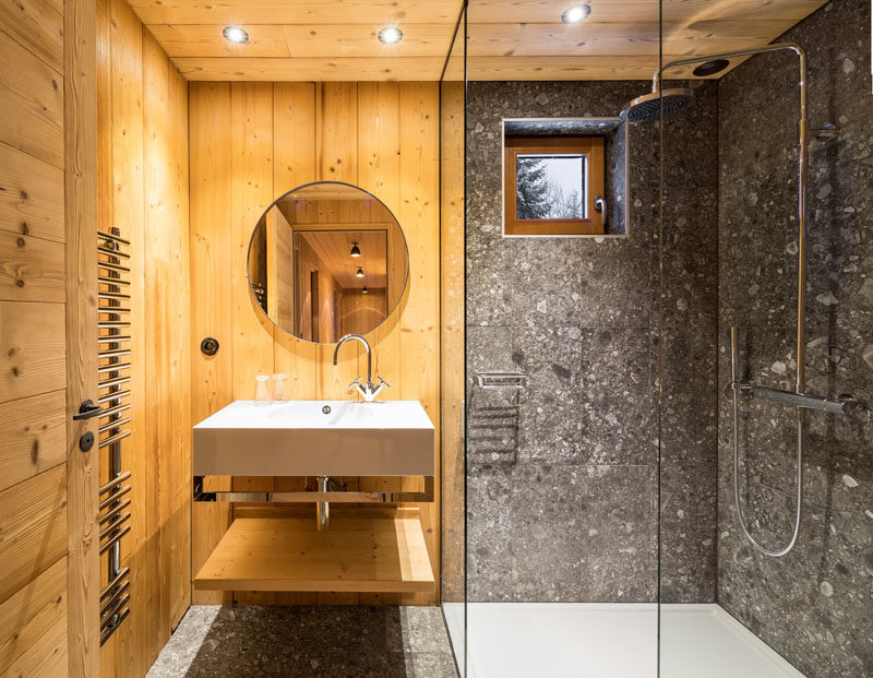 In this rustic modern bathroom, wood walls and ceiling have been paired with stone tiles and a glass shower partition.