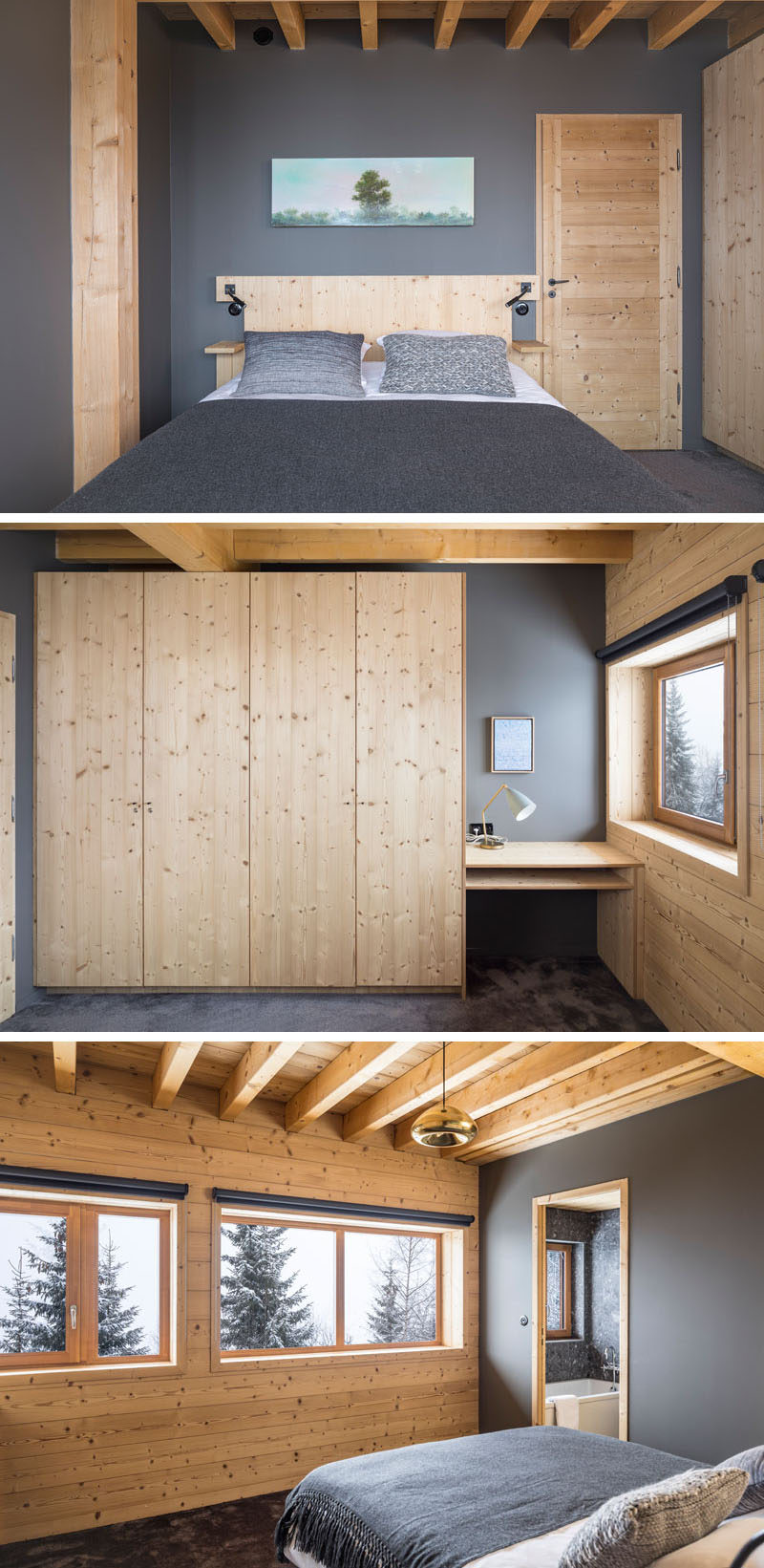 This rustic modern bedroom features dark grey accent walls, a large wood closet and desk, and windows with mountain views.