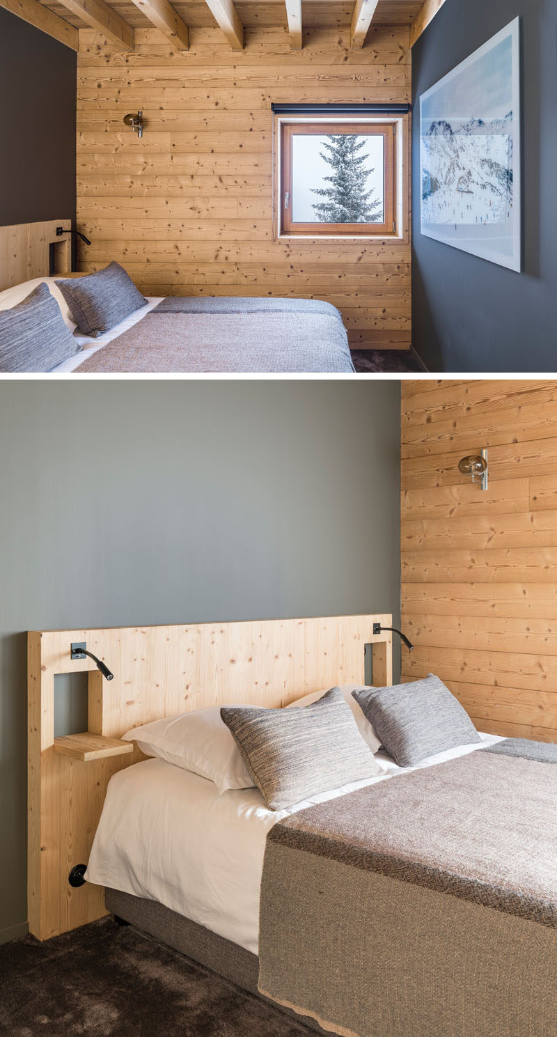 This rustic modern bedroom features dark grey accent walls, a custom wood headboard, and a square window with mountain views.
