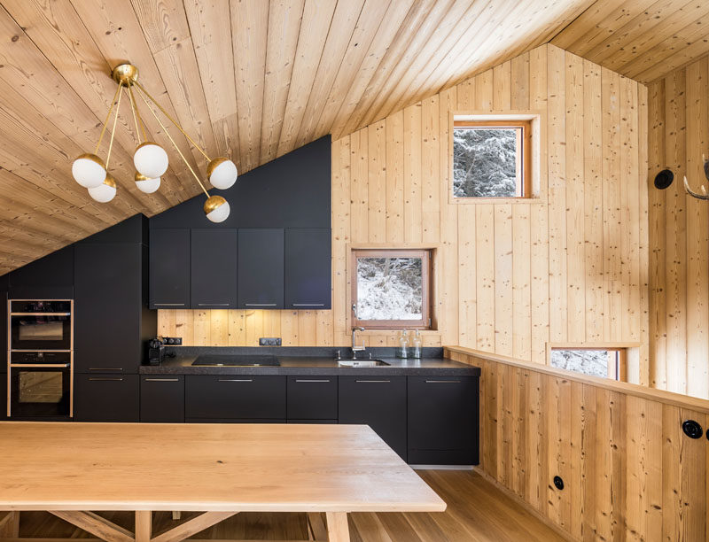 At the top of the stairs in this modern mountain house is the kitchen. Matte black kitchen cabinets fill the wall and follow the sloped roof line.