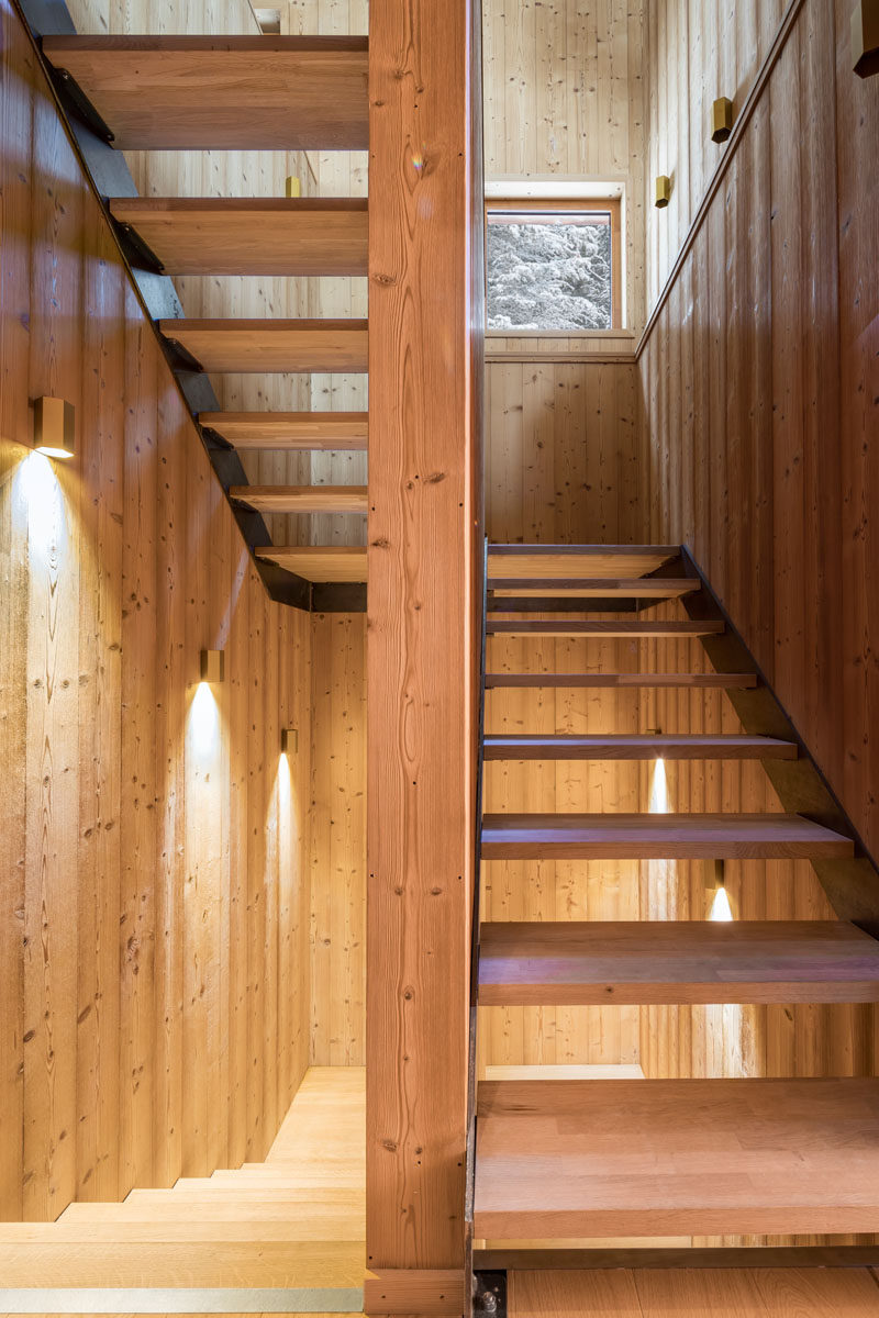 This modern mountain house has wood stairs that connect the various levels of the home, while wall sconces and square windows allow light to fill the stairwell.