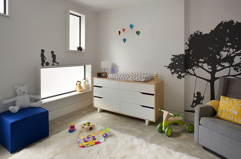 In this modern nursery, rectangular opaque windows glow from the light in the living area, while wall decals of children playing add a touch of fun to the room.