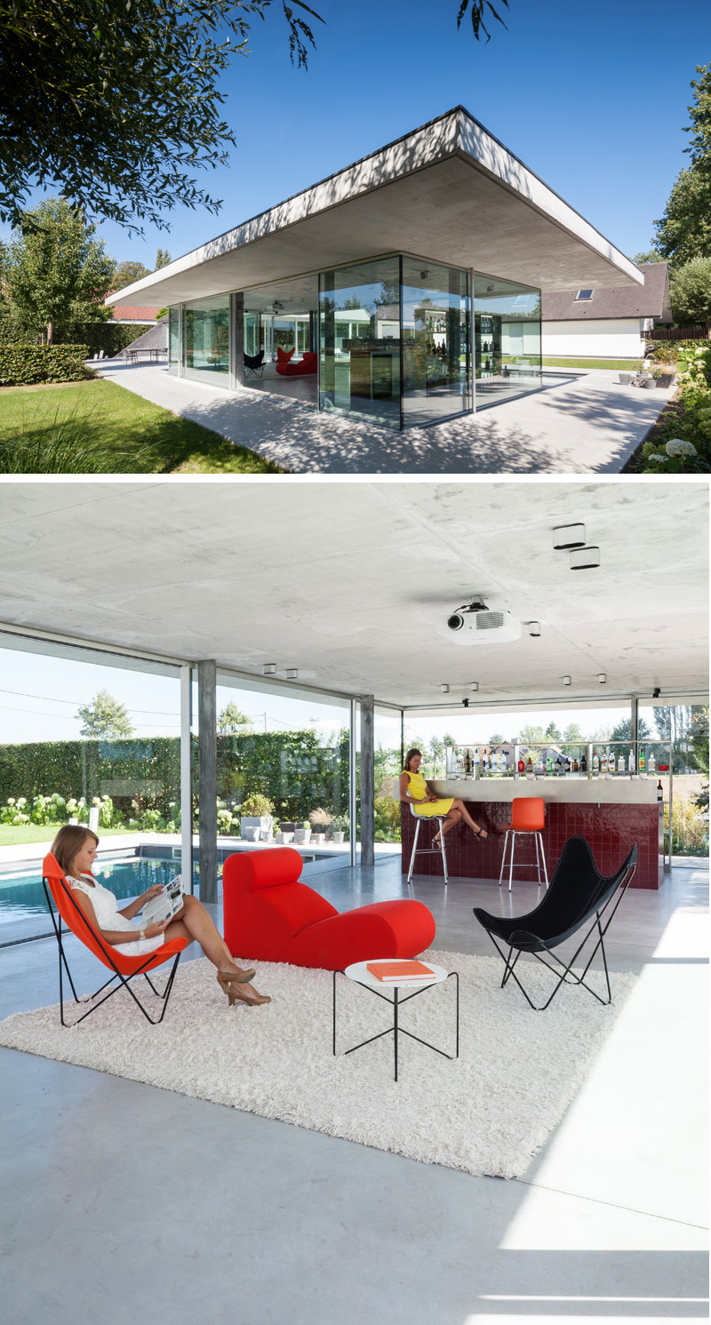 Surrounded by glass, this modern concrete pool house provides a great view of outside. A red tiled bar, and cozy seating make this a great place to have a drink after a dip in the pool.