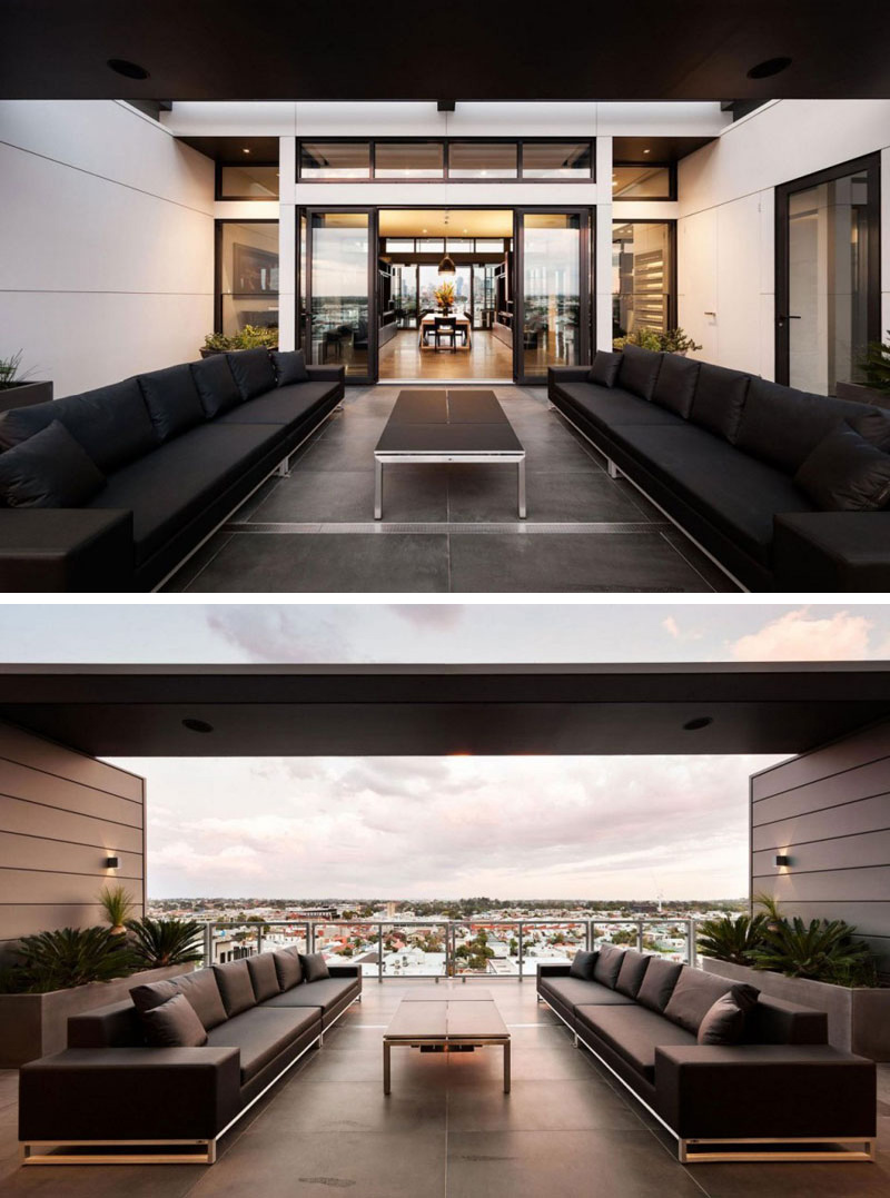 This modern outdoor balcony has an unobstructed view of the city. Two large black sofas provide more than enough room for guests.