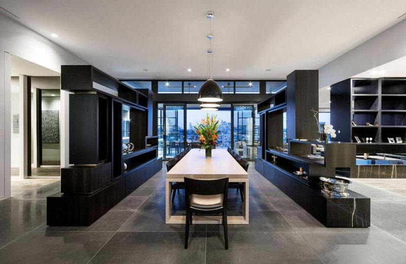 Inside this modern penthouse, a large white dining table sits below three black pendant lights, and divides different areas of the home.