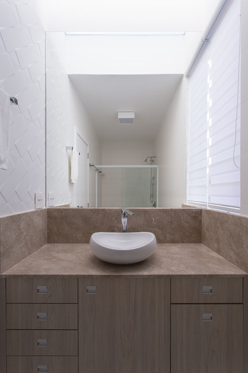 In this modern bathroom, a decorative white tile on the wall adds texture, while the large mirror helps to make the small space appear larger than it is.