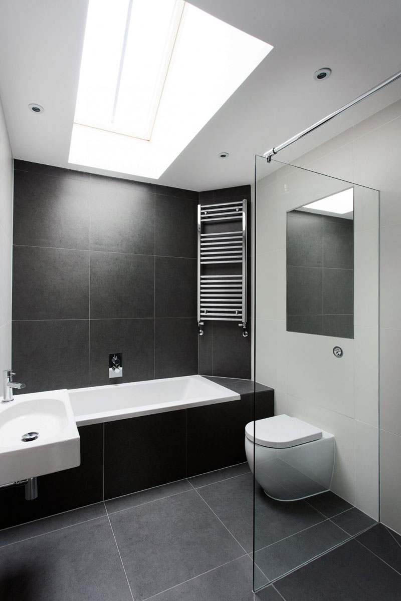 In this modern bathroom, a skylight shines light on to the large dark grey tiles used throughout, and a glass wall separates the shower area from the rest of room.