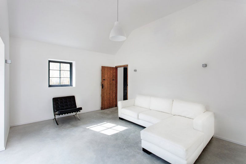 This modern living room is full of open space and is minimally decorated. The smooth concrete floor, white pendant light, and the white and black furniture keeps this space simple.