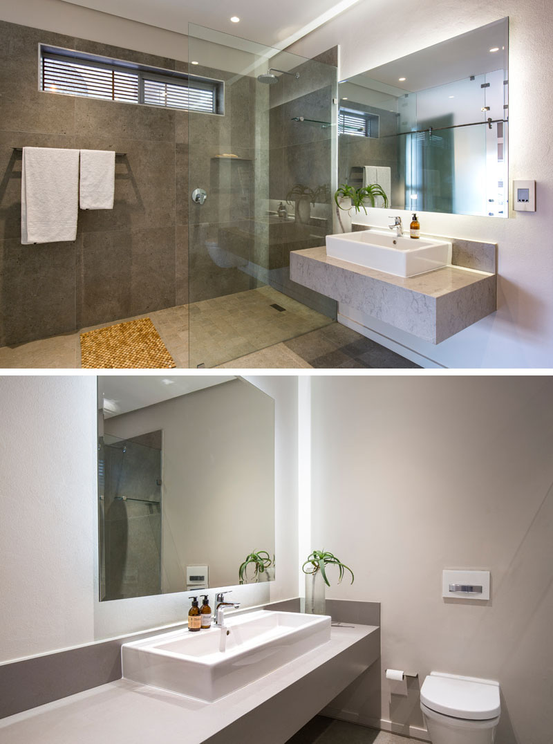 The large shower in this modern bathroom is defined by the stone tiles and glass shower surround. Next to the shower is a floating vanity and backlit rectangular mirror. Off to the side, a separate space is provided for the the toilet.