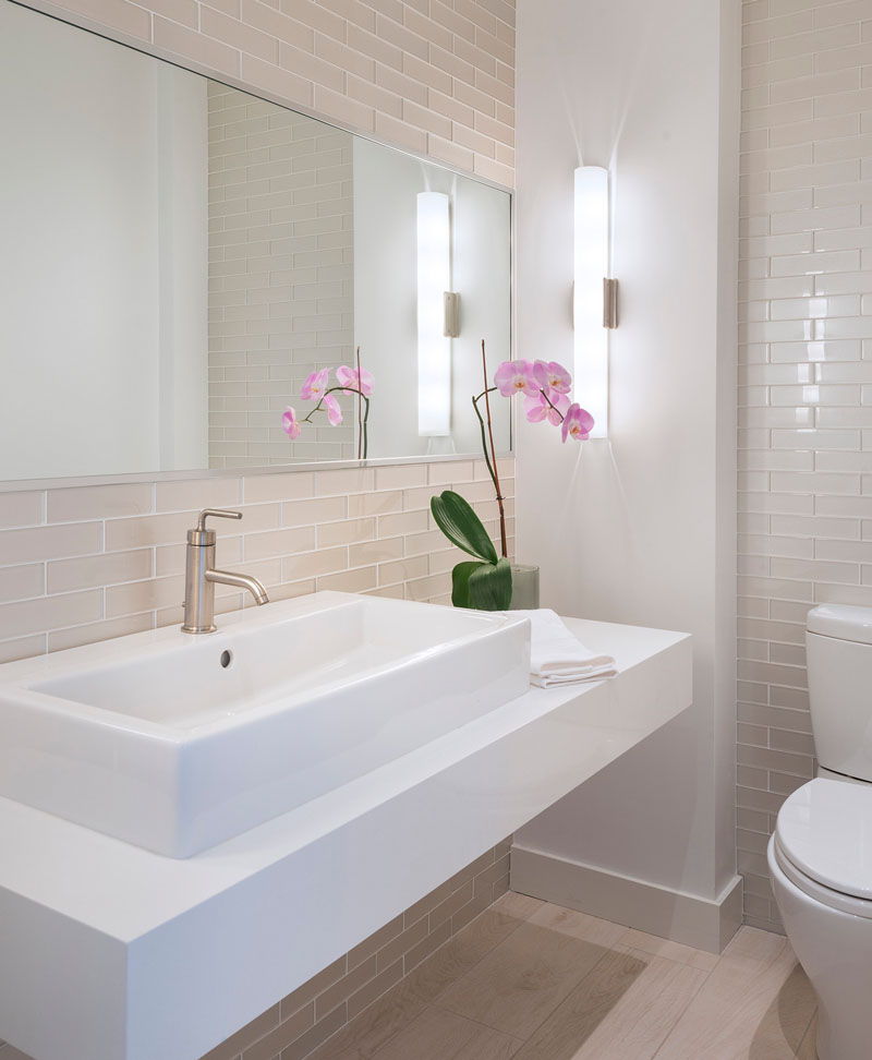 Light pink rectangular tiles cover the walls in this modern bathroom that also has light wood flooring, while a floating white vanity sits below a large mirror.