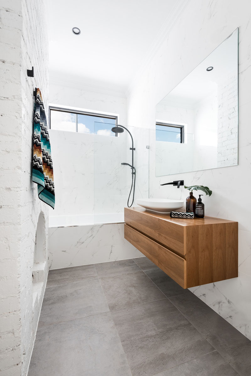 In this renovated bathroom, an original fireplace has been left as a design feature, while the rest of the bathroom has been updated with a large mirror and floating wood vanity.