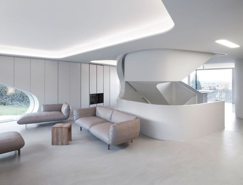 Arriving to the second level of the house, the recessed ceiling in this modern living room has hidden lighting making this white room even brighter. Light colored upholstered furniture, and a small wood coffee table sits comfortably on the bare concrete floor. 