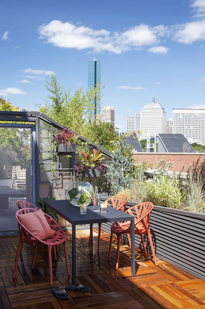 This modern wood balcony is furnished with a black table, and bright orange chairs. The potted plants in this space don't interfere with the spectacular view of the city. 