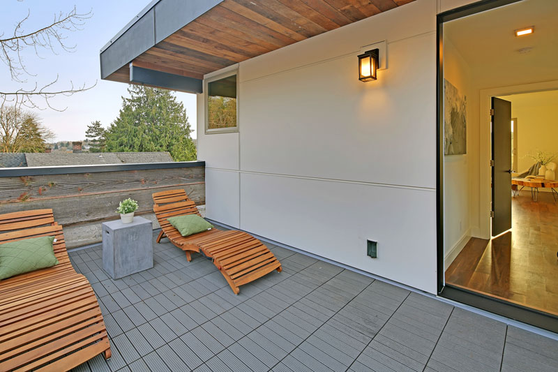 At the top of this modern house is a private sun deck with two wood sun chairs.