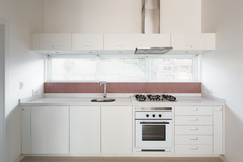 In this small kitchen, simple white cabinets almost blend in with the white walls, while the backsplash provides a dash of red.