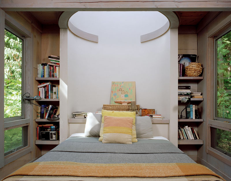 This bedroom inside a modern cabin features built-in shelving and windows on either side of the bed.