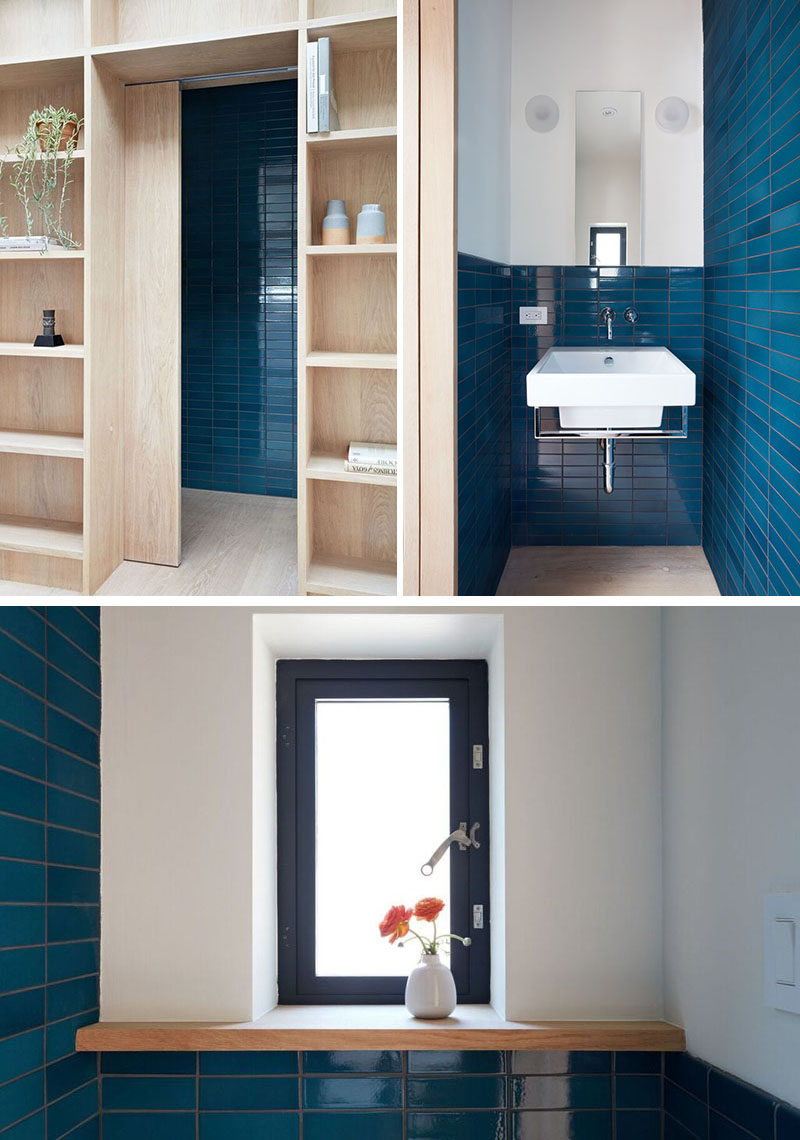 Hidden within the wall of shelves in this modern backyard studio, is a door that opens to reveal a powder room, that features bold blue tiles. 