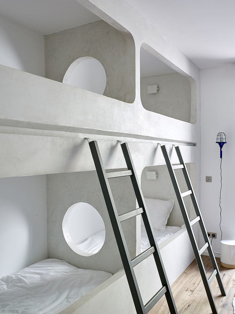 In this modern bedroom in a holiday house, a set of two bunk beds have been custom built into the design of the room. The center wall that separates the bunks has a round hole so that people can easily see and talk to each other.