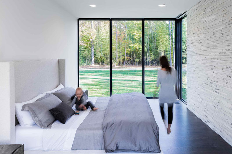 This modern master bedroom looks out onto the yard through floor-to-ceiling windows and features a stone accent wall.